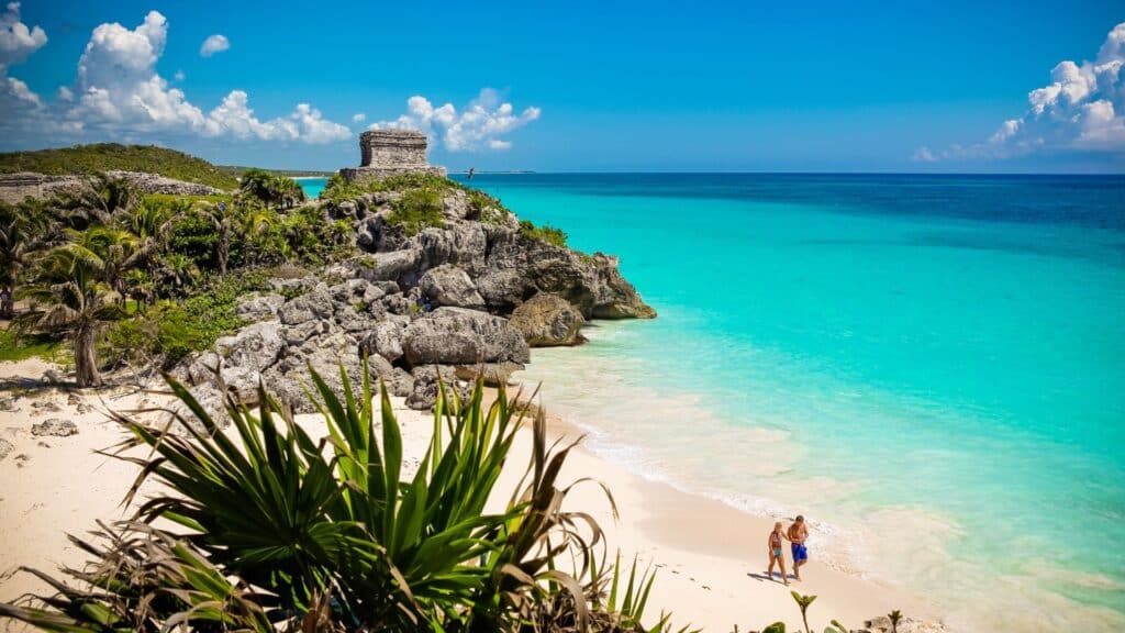 Couple enjoys walking on the beach in Tulum with Ruins in the background
